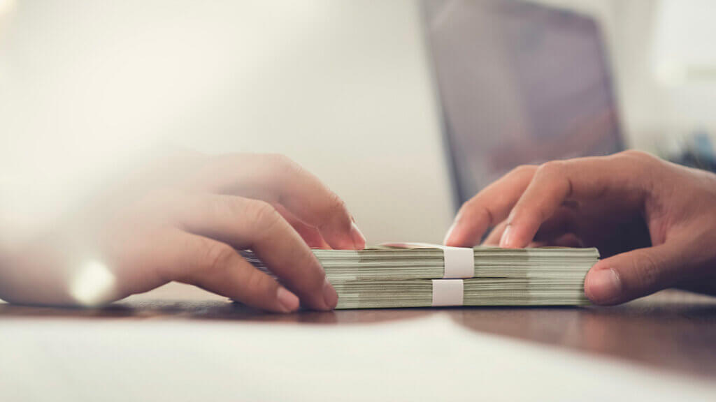 Two sets of hands exchanging thick stacks of dollar bills on wooden surface representing direct lending.