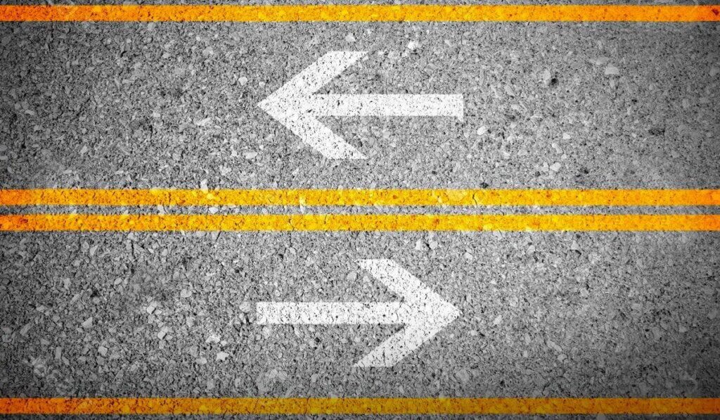 Two white arrows on gray pavement pointing left and right with yellow road lines representing lease versus loan choice.