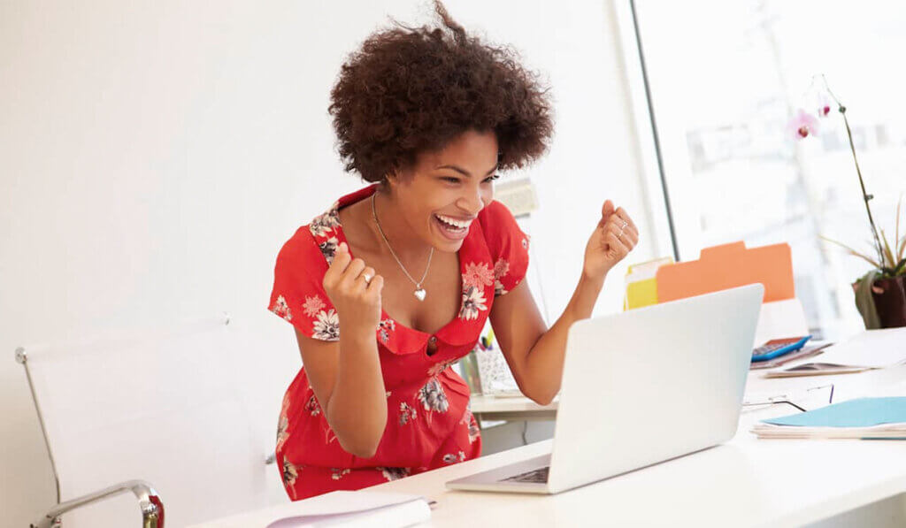 Smiling woman with curly hair raising fists in celebration while looking at laptop displaying credit rating information.
