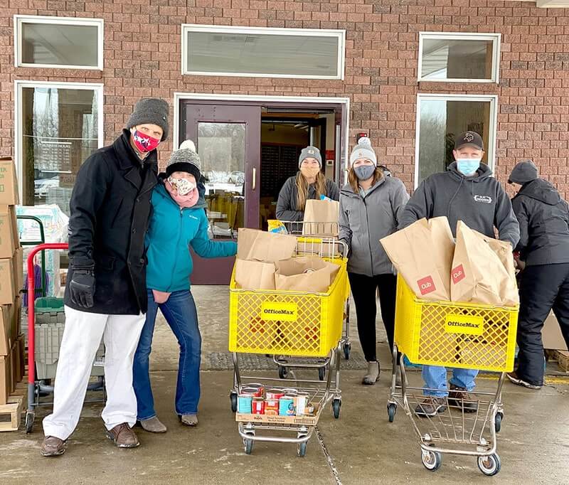 Seven people wearing masks and winter clothing standing with yellow shopping carts full of food donation bags.