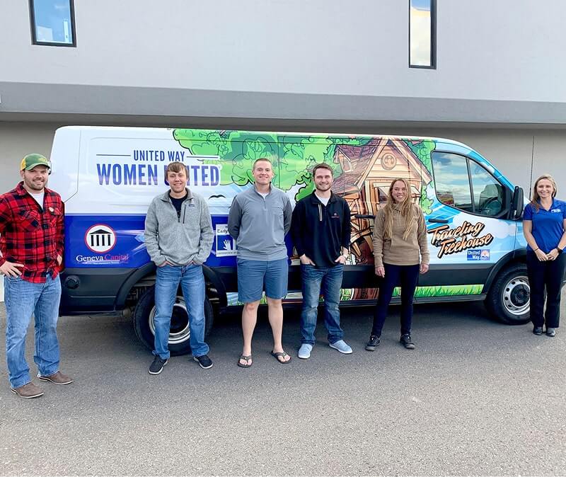 Six people posing next to colorful United Way Women United van with Geneva Capital branding on side.