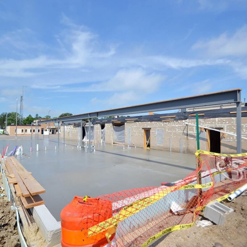 Construction site with partially completed building structure, orange safety barriers, and construction equipment under blue sky.