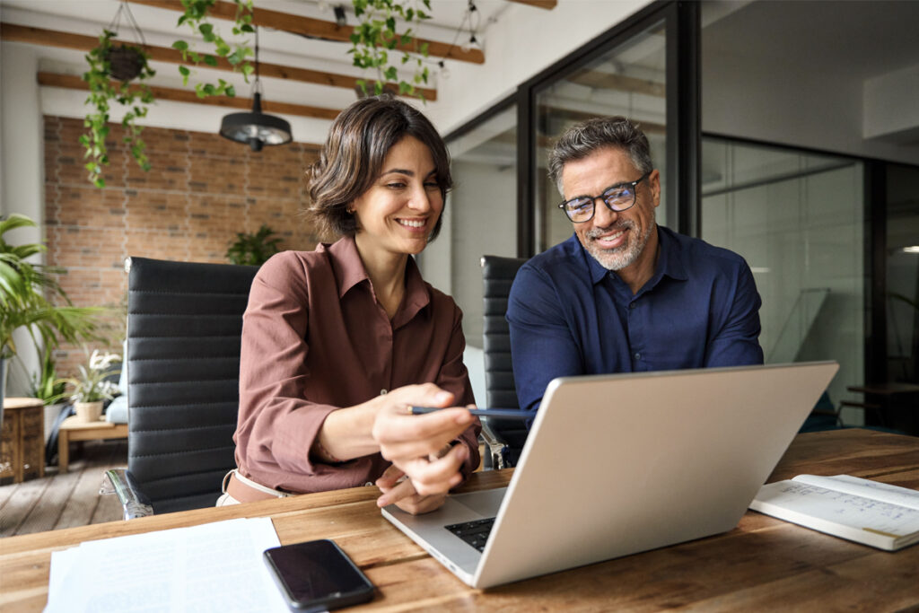 Man and woman looking at a computer screen while the woman points and explains something to the man.
