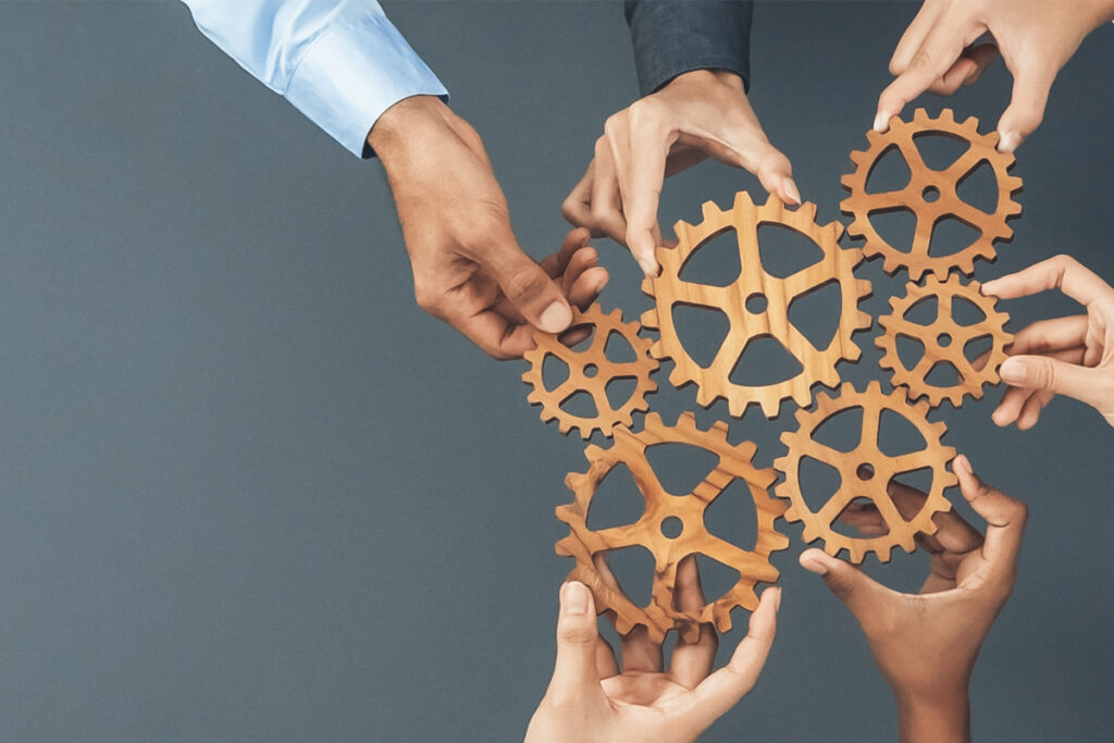 Hands assembling wooden gears on a blue background.