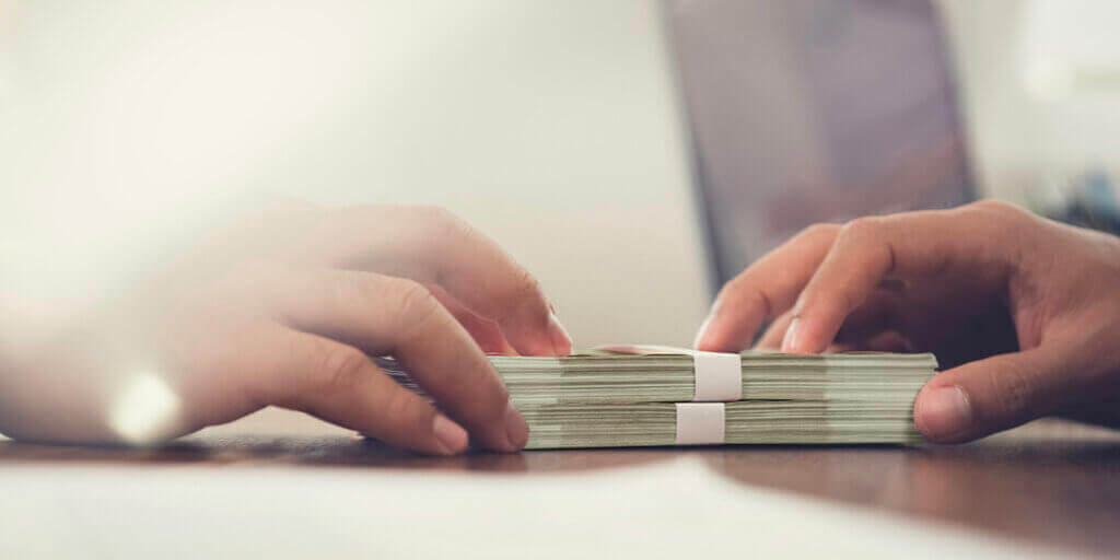 Two sets of hands exchanging thick stacks of dollar bills on wooden surface representing direct lending.