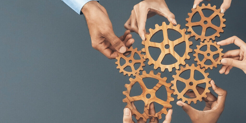 Hands assembling wooden gears on a blue background.