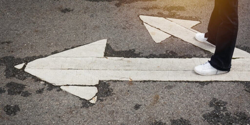 White sneakers standing on broken white arrows painted on asphalt road showing different lease directions.