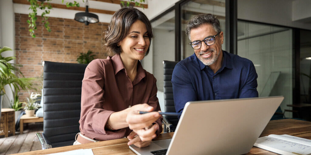 Man and woman looking at a computer screen while the woman points and explains something to the man.