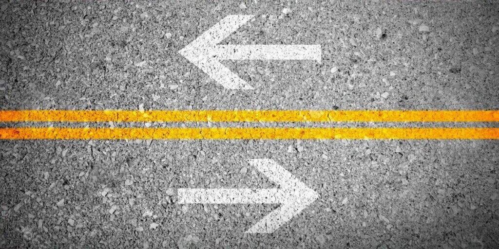 Two white arrows on gray pavement pointing left and right with yellow road lines representing lease versus loan choice.