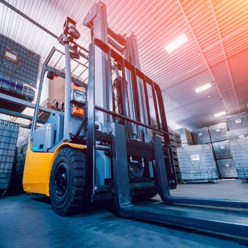 Industrial forklift with extended mast in warehouse setting with high shelving and palletized goods.