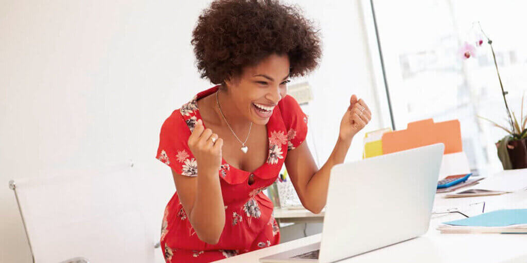 Smiling woman with curly hair raising fists in celebration while looking at laptop displaying credit rating information.