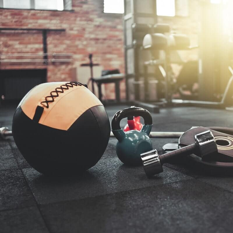 Orange and black medicine ball with kettlebell and dumbbells on dark gym floor.