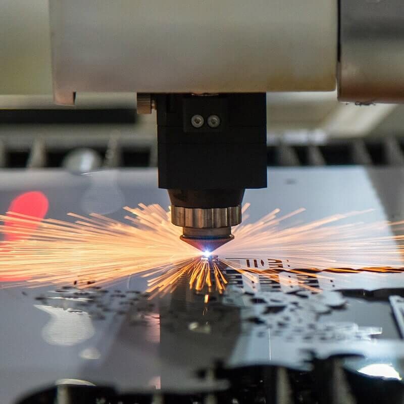 Laser cutting machine head producing bright sparks while cutting metal sheet in industrial manufacturing setting.Retry
