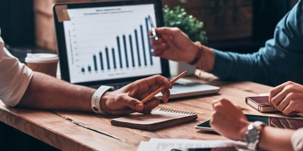 Hands pointing at tablet showing bar chart while reviewing lease documents and paperwork on desk.
